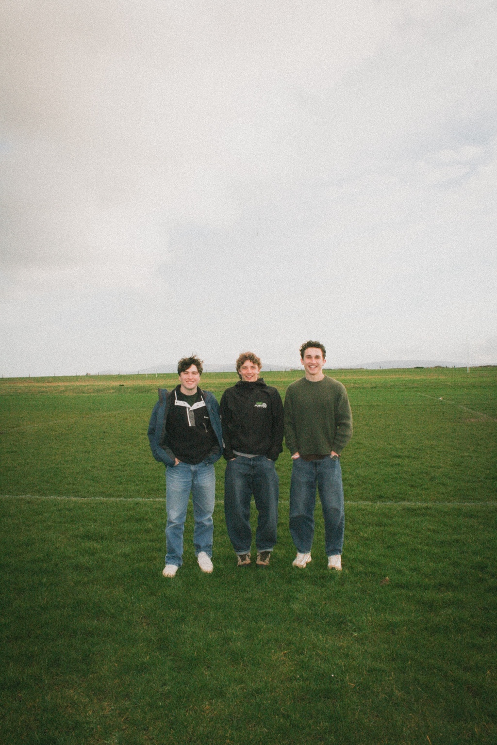 Three friends standing in a grassy field