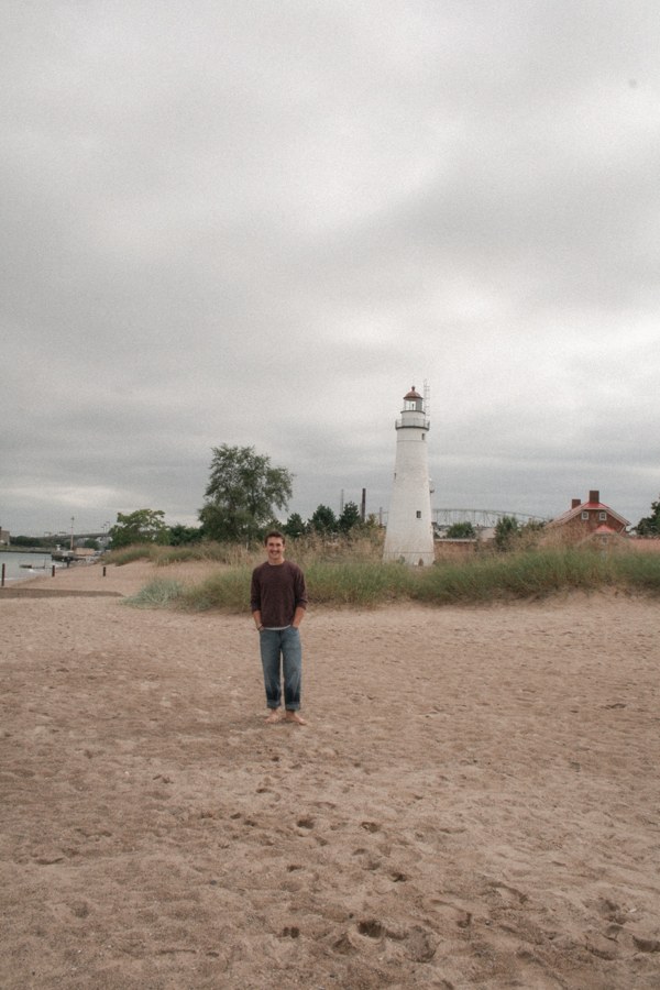 Figure walking toward a lighthouse on a cloudy beach